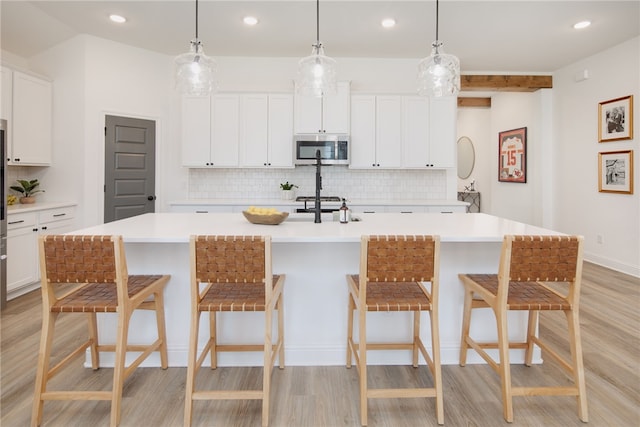 kitchen with light countertops, stainless steel microwave, a kitchen island with sink, and white cabinetry