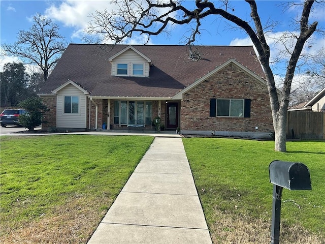 view of front of house with roof with shingles, fence, a front lawn, and brick siding