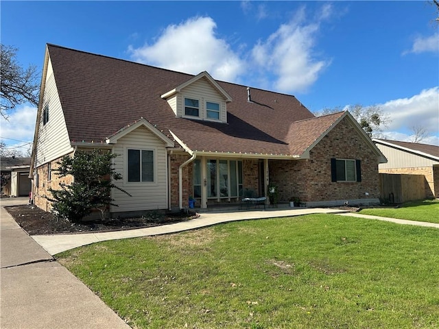 new england style home with a front lawn, roof with shingles, and brick siding