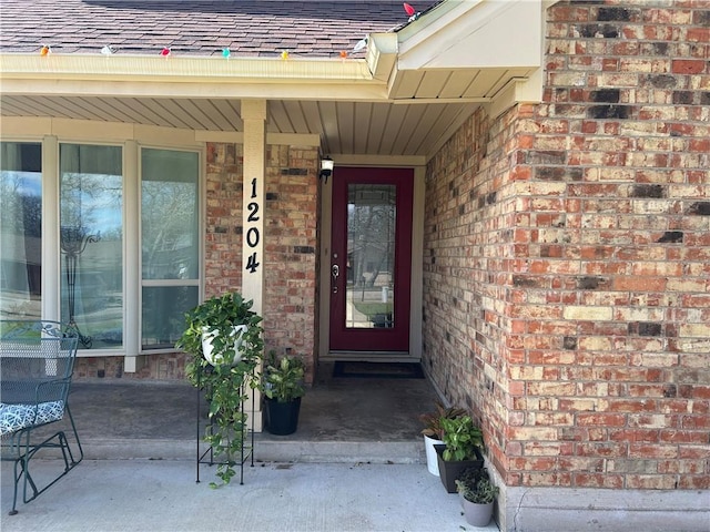 view of exterior entry featuring a shingled roof and brick siding