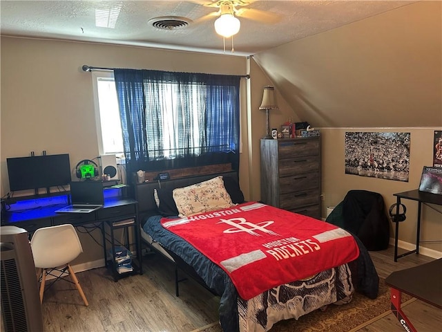 bedroom with a textured ceiling, wood finished floors, visible vents, baseboards, and vaulted ceiling