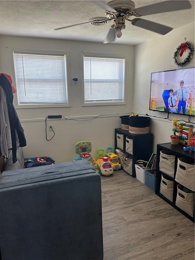 game room with ceiling fan, plenty of natural light, a textured ceiling, and wood finished floors