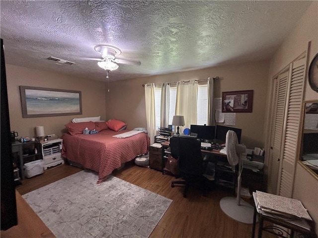 bedroom with a closet, visible vents, a textured ceiling, and wood finished floors