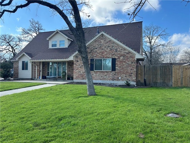 view of front of property featuring roof with shingles, fence, a front lawn, and brick siding