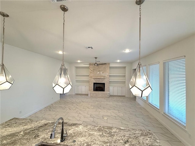 unfurnished living room with ceiling fan, sink, built in features, and a fireplace