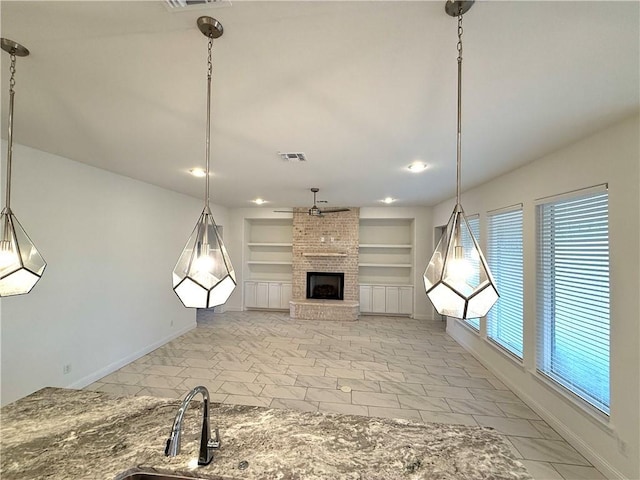 unfurnished living room featuring built in shelves, ceiling fan, sink, and a brick fireplace