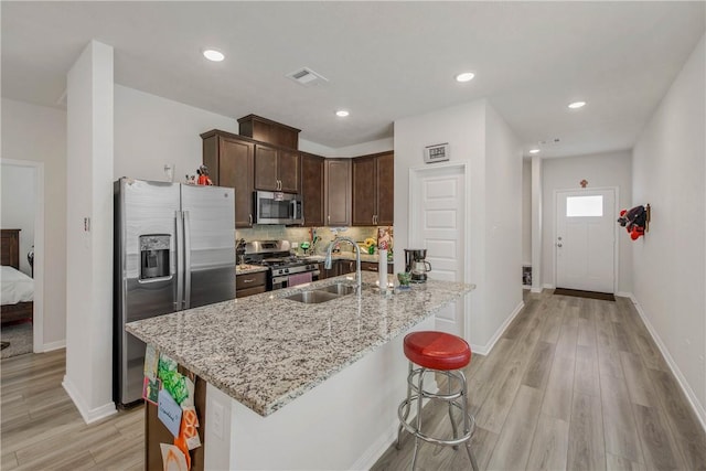 15213 Still Water Meadow Loop, College Station, TX 77845 - kitchen featuring stainless steel appliances, a sink, light stone counters, light wood-style flooring, and dark brown cabinetry
