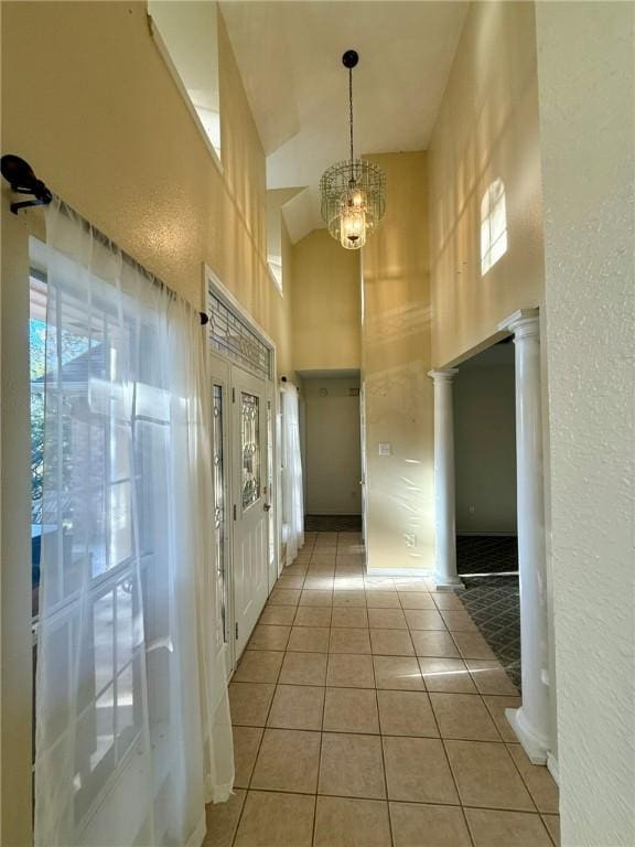 corridor with light tile patterned floors, a towering ceiling, and an inviting chandelier