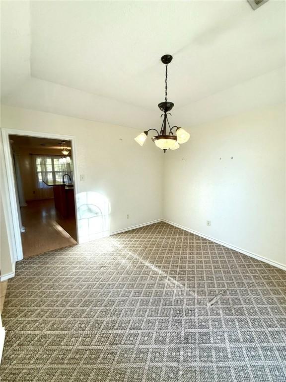 carpeted spare room with a chandelier