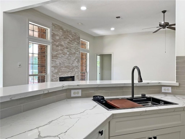 kitchen featuring sink, ceiling fan, white cabinetry, light stone counters, and ornamental molding