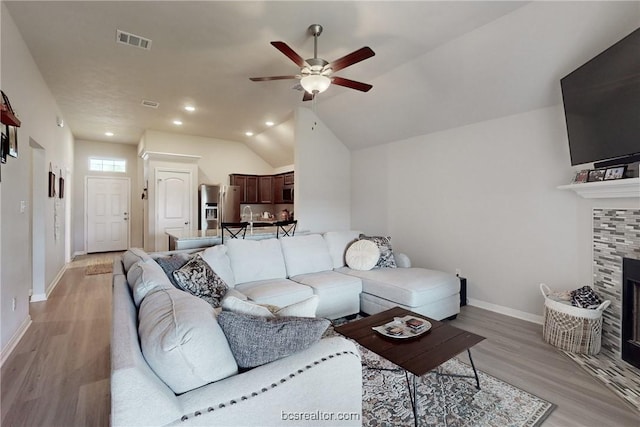 living room featuring a tile fireplace, light hardwood / wood-style floors, vaulted ceiling, and ceiling fan