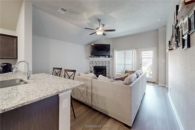 living room featuring light wood-type flooring, vaulted ceiling, ceiling fan, sink, and a tile fireplace