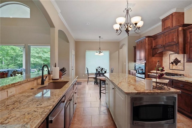 kitchen featuring sink, stainless steel appliances, light stone counters, a notable chandelier, and an island with sink