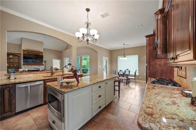 kitchen featuring appliances with stainless steel finishes, light stone counters, dark brown cabinets, an inviting chandelier, and a center island