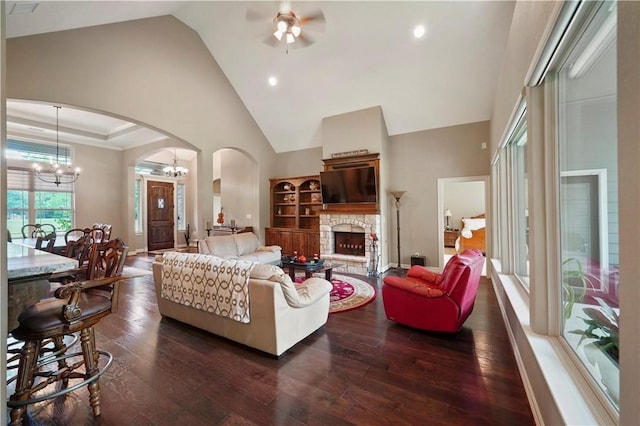 living room featuring a stone fireplace, dark hardwood / wood-style flooring, high vaulted ceiling, and ceiling fan with notable chandelier