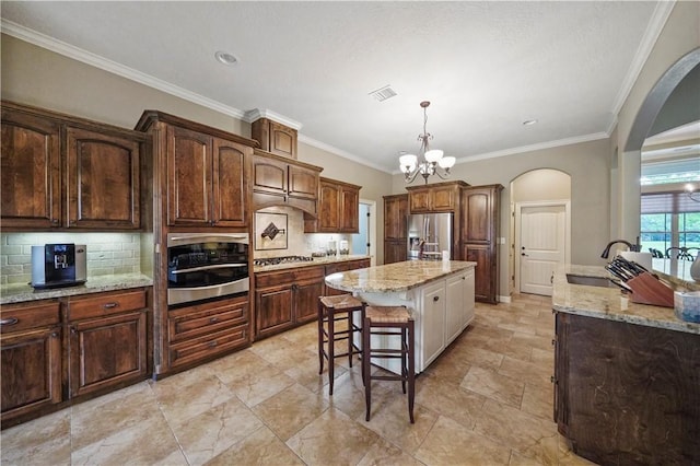 kitchen featuring light stone countertops, sink, a center island, decorative light fixtures, and appliances with stainless steel finishes