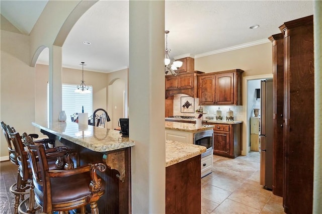 kitchen featuring tasteful backsplash, light stone counters, pendant lighting, an inviting chandelier, and a breakfast bar area