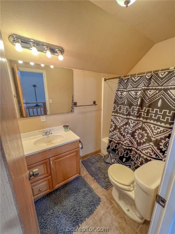 full bathroom with shower / bathtub combination with curtain, tile patterned floors, vaulted ceiling, toilet, and vanity