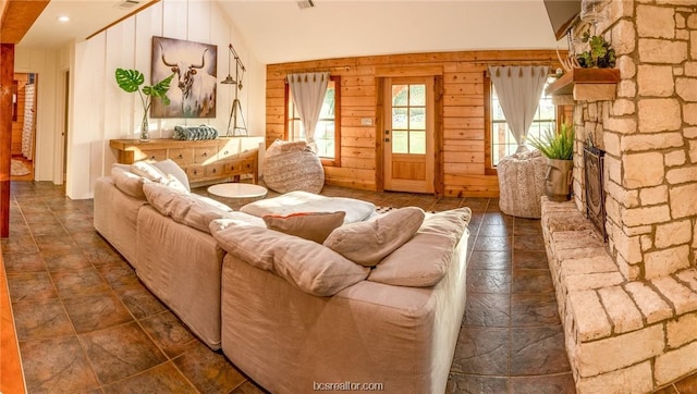 living room featuring a stone fireplace, wooden walls, and vaulted ceiling