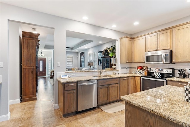 kitchen with sink, backsplash, light stone counters, kitchen peninsula, and stainless steel appliances