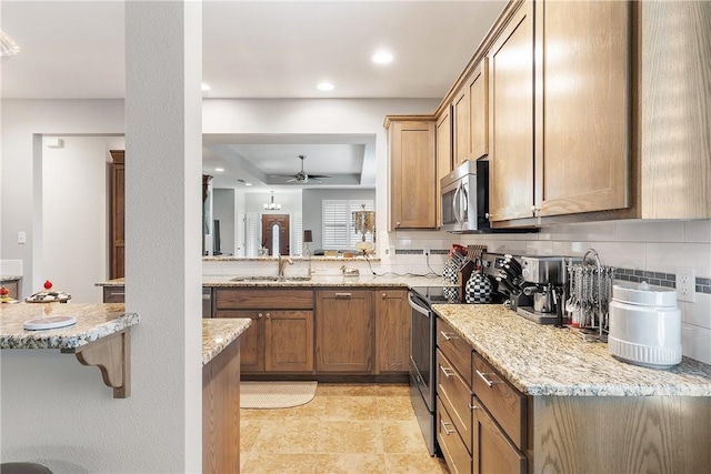 kitchen featuring sink, backsplash, stainless steel appliances, light stone countertops, and a raised ceiling