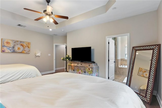 bedroom featuring ceiling fan, ensuite bath, and a tray ceiling