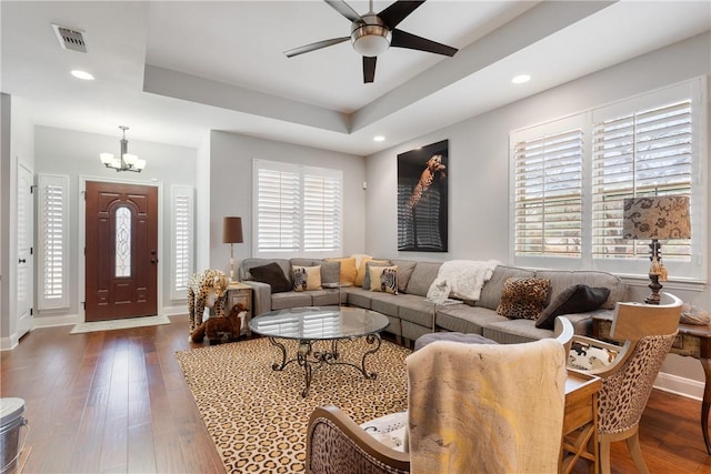 living room with dark hardwood / wood-style floors, a raised ceiling, and ceiling fan with notable chandelier