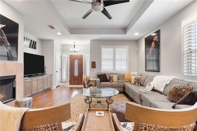 living room featuring a tray ceiling, a tile fireplace, a healthy amount of sunlight, and light wood-type flooring