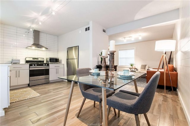 kitchen with white cabinetry, wall chimney range hood, stainless steel appliances, decorative backsplash, and light wood-type flooring