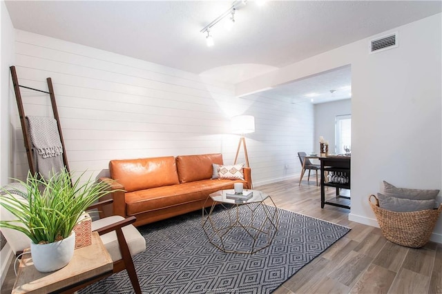 living room with rail lighting, wood walls, and hardwood / wood-style flooring