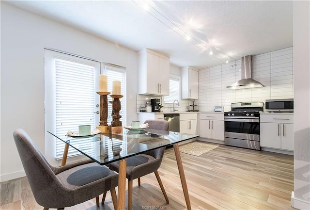 kitchen with light hardwood / wood-style floors, decorative backsplash, stainless steel appliances, white cabinets, and wall chimney exhaust hood