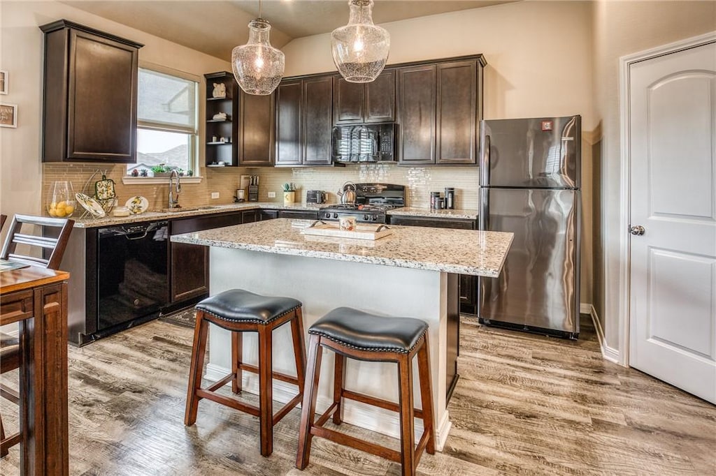 kitchen featuring dark brown cabinetry, black appliances, decorative light fixtures, a center island, and light hardwood / wood-style floors