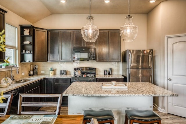 kitchen with a center island, black appliances, sink, hanging light fixtures, and light stone countertops