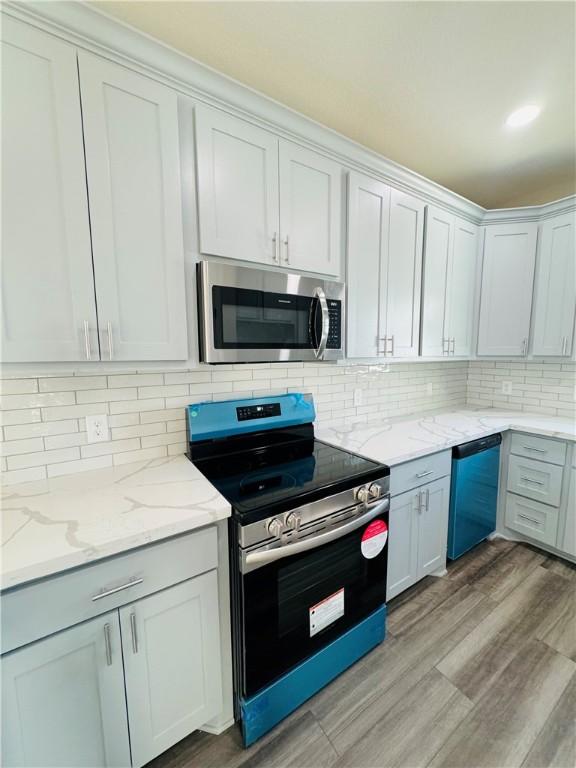 kitchen featuring light stone counters, light hardwood / wood-style flooring, appliances with stainless steel finishes, decorative backsplash, and white cabinets