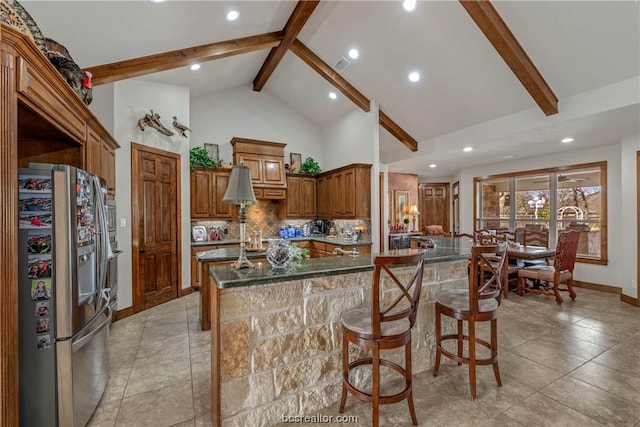 kitchen with stainless steel fridge, backsplash, a breakfast bar, a center island with sink, and beamed ceiling