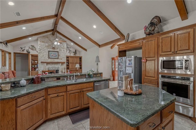 kitchen with a stone fireplace, sink, appliances with stainless steel finishes, a large island, and beam ceiling