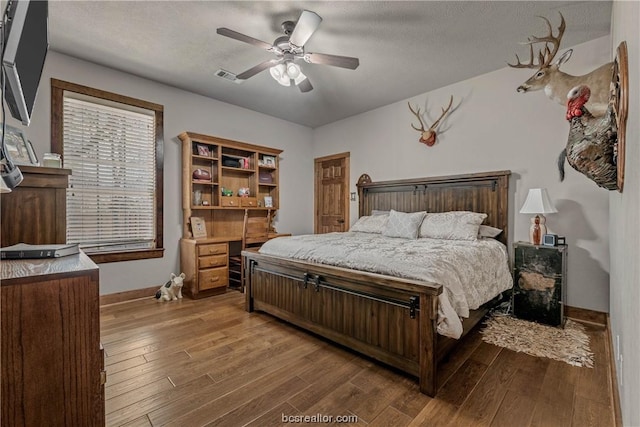 bedroom with ceiling fan, wood-type flooring, and a textured ceiling