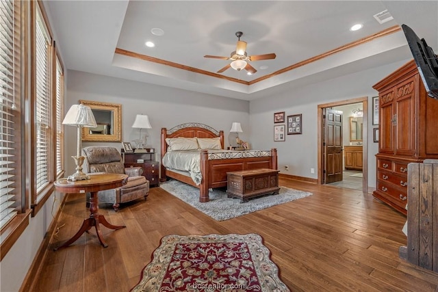 bedroom with light wood-type flooring, ensuite bath, a tray ceiling, ceiling fan, and crown molding