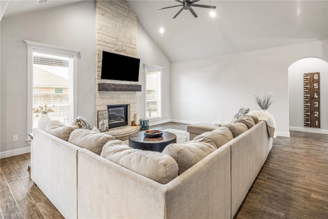 living room with dark wood-type flooring, high vaulted ceiling, a stone fireplace, and a wealth of natural light