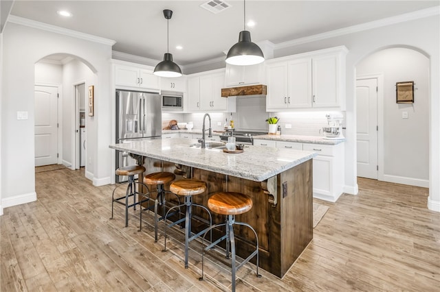 kitchen featuring a center island with sink, appliances with stainless steel finishes, light hardwood / wood-style floors, white cabinets, and light stone countertops