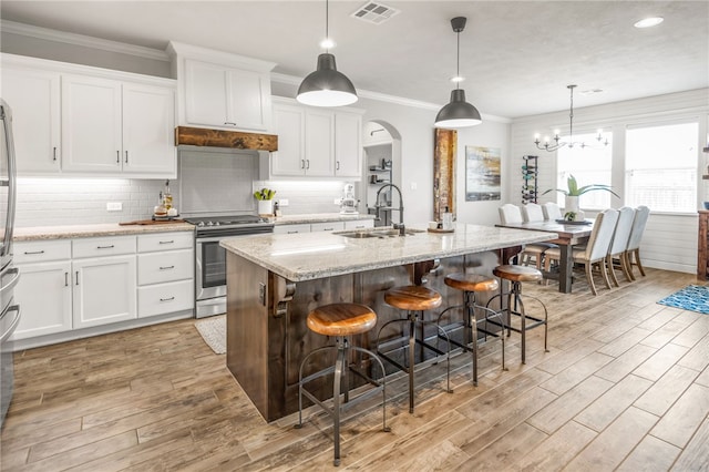 kitchen with sink, light stone counters, white cabinetry, stainless steel electric stove, and a kitchen island with sink