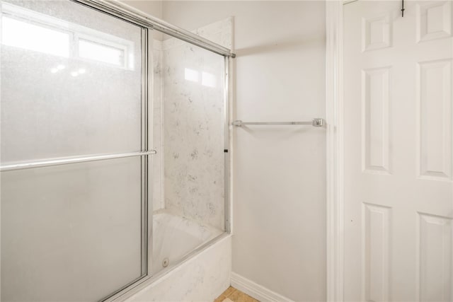 bathroom featuring baseboards and bath / shower combo with glass door