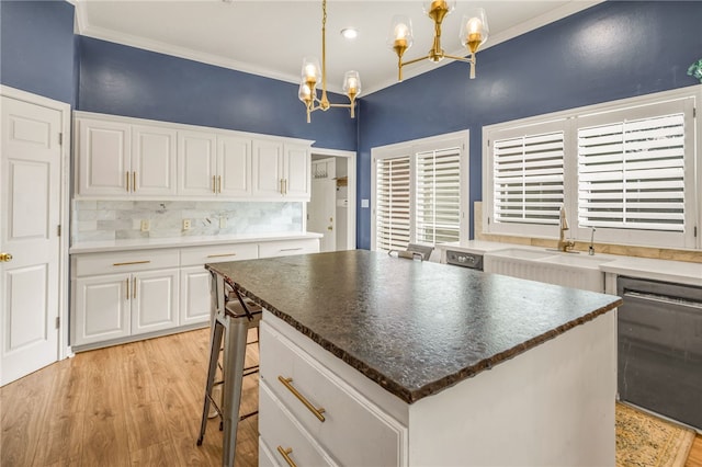 kitchen with tasteful backsplash, light wood-style floors, white cabinets, a sink, and a notable chandelier