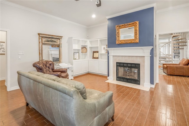 living room featuring a tiled fireplace, ceiling fan, baseboards, ornamental molding, and wood finished floors