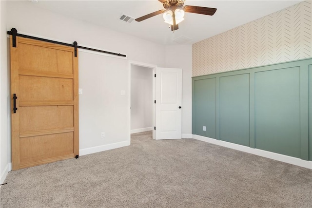 unfurnished bedroom with light carpet, a barn door, a closet, and ceiling fan