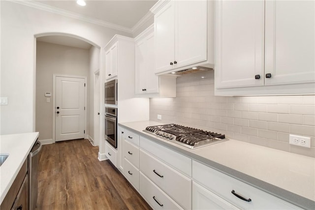 kitchen featuring dark wood-type flooring, ornamental molding, tasteful backsplash, white cabinetry, and stainless steel appliances