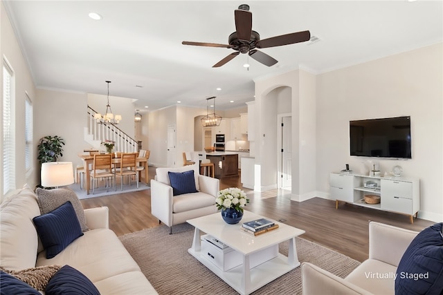 living room with ceiling fan with notable chandelier, light hardwood / wood-style flooring, and crown molding