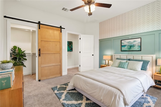 carpeted bedroom featuring a barn door and ceiling fan