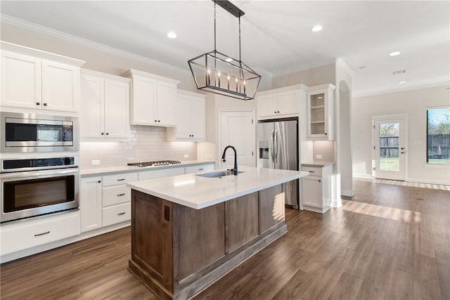 kitchen featuring ornamental molding, stainless steel appliances, a kitchen island with sink, sink, and white cabinets