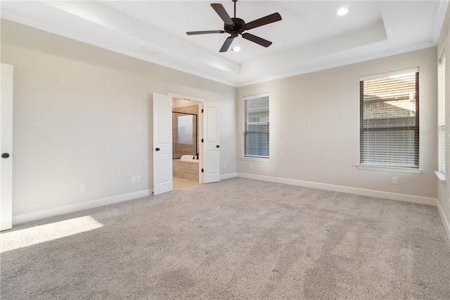 unfurnished bedroom featuring a raised ceiling, ensuite bathroom, carpet flooring, and ceiling fan